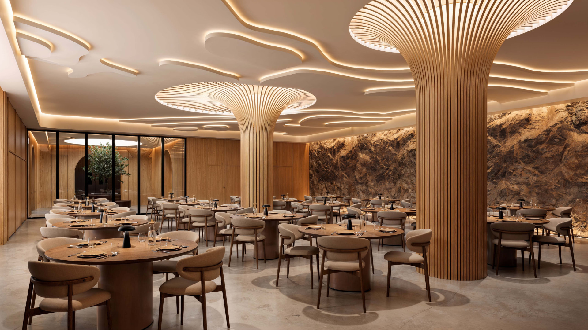 Developer rendering of an underground dining room with round tables, sculpted timber columns fanning into illuminated ceiling discs and a rock wall