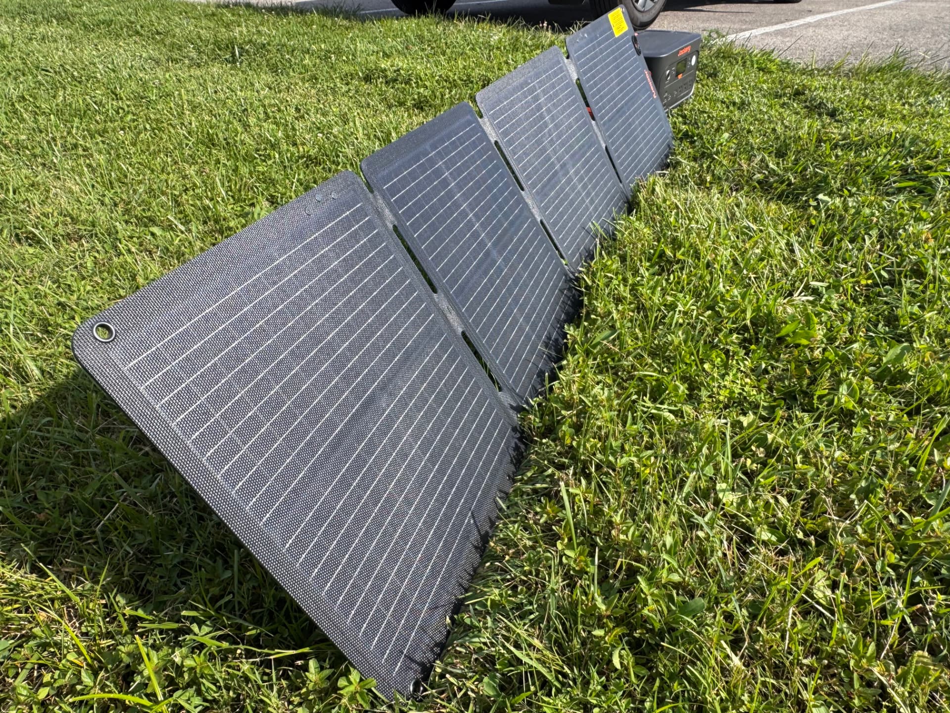 Close-up of folding solar panels laid out in grass connected to a Jackery power station