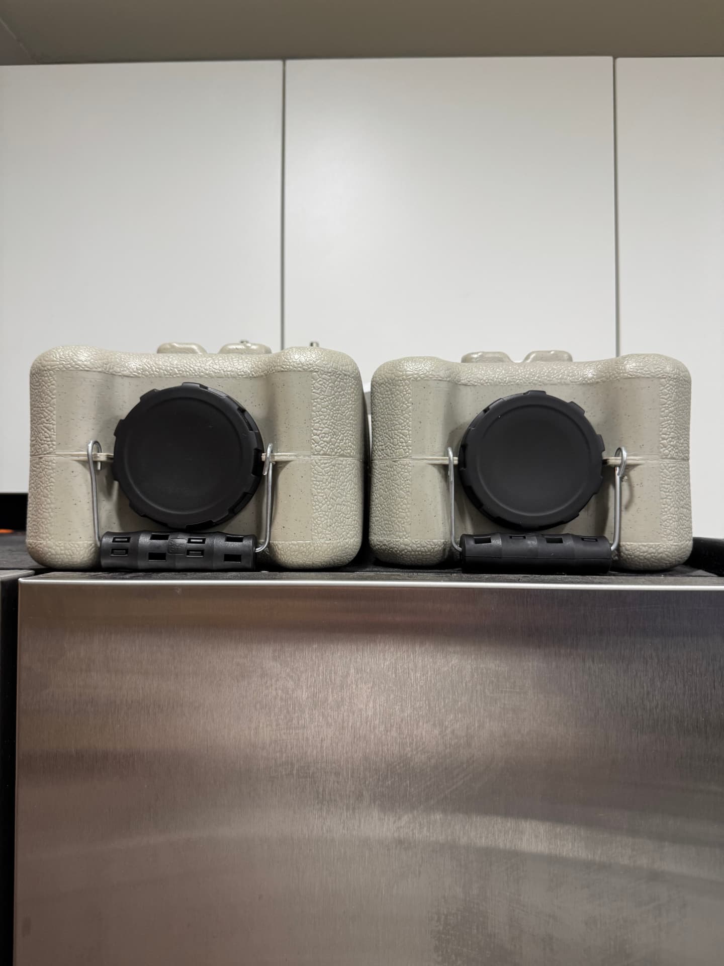 Two earth-tone WaterBrick containers side by side showing black screw caps and wire-bail carry handles