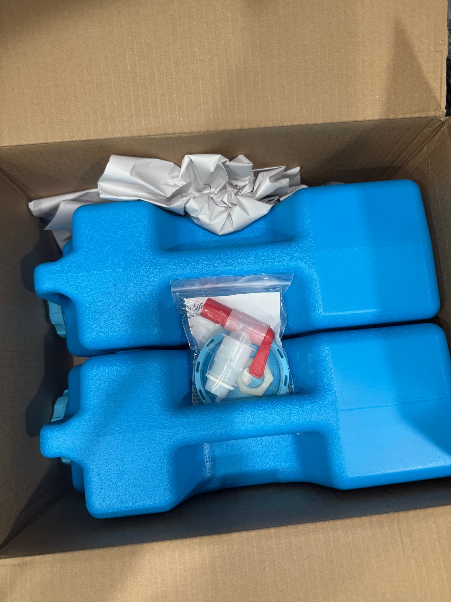 Two blue AquaBrick containers packed snugly in a shipping box with a bagged spigot kit