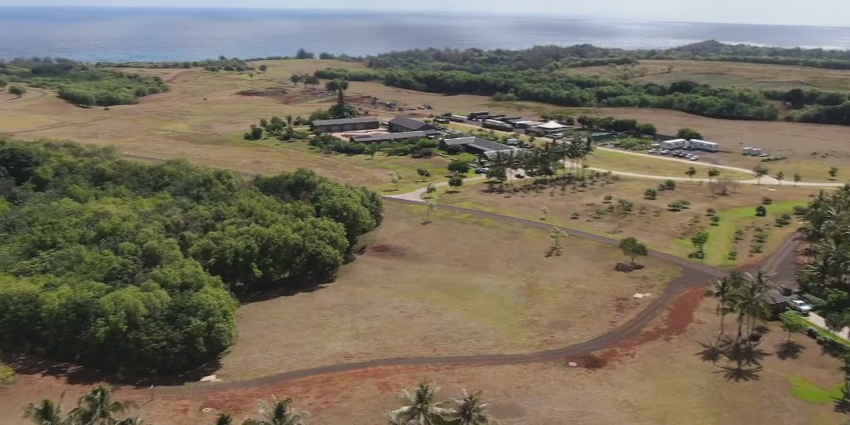 Aerial view of a large coastal ranch property in Hawaii with scattered buildings, tree lines and open pasture running down to the ocean