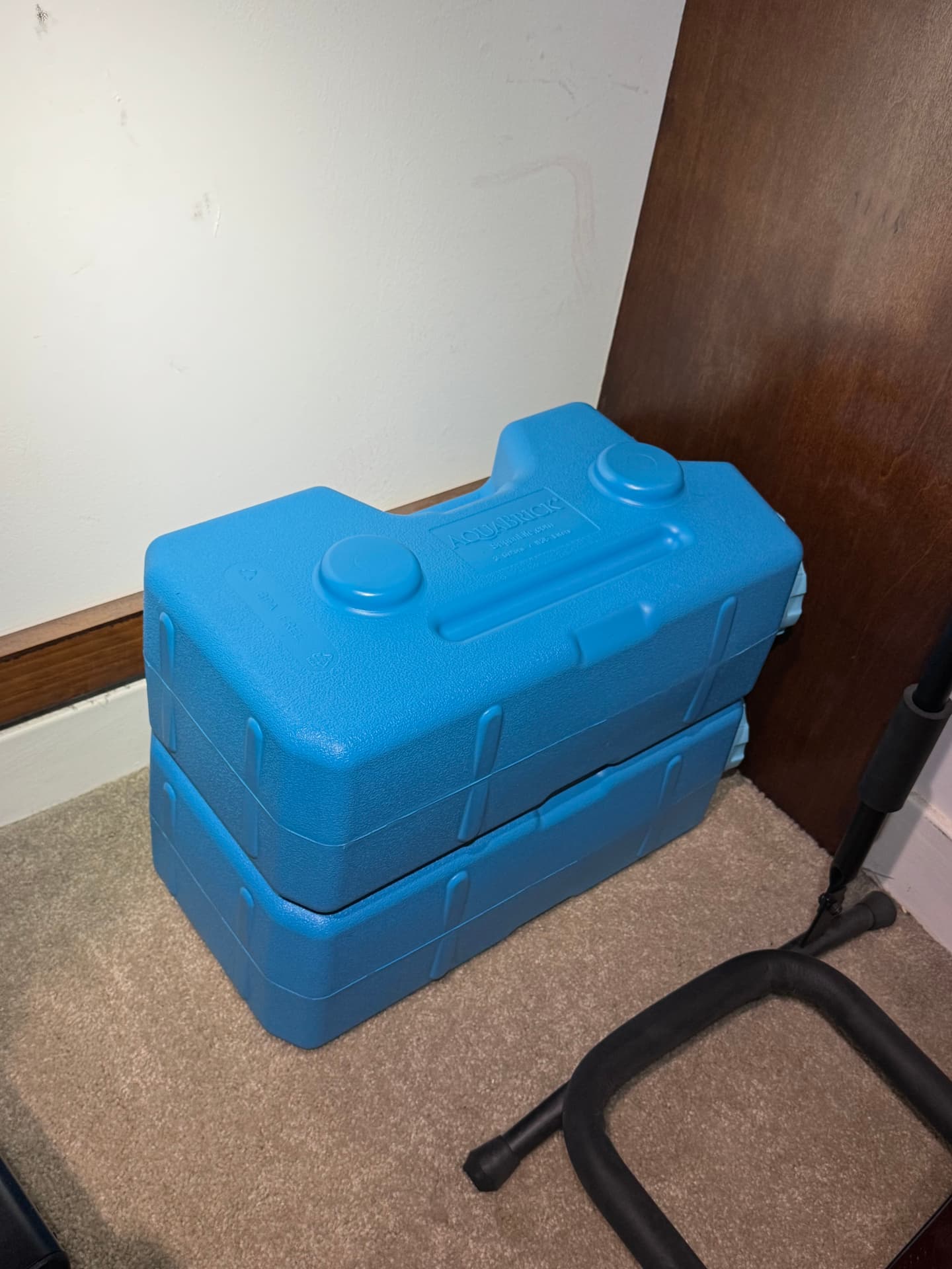 Two blue AquaBrick containers stacked on the floor against a wall, showing molded top handles