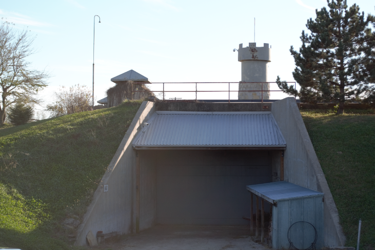 Concrete entry ramp leading down into the earth-covered Subterra Castle bunker, with the stone watchtower above