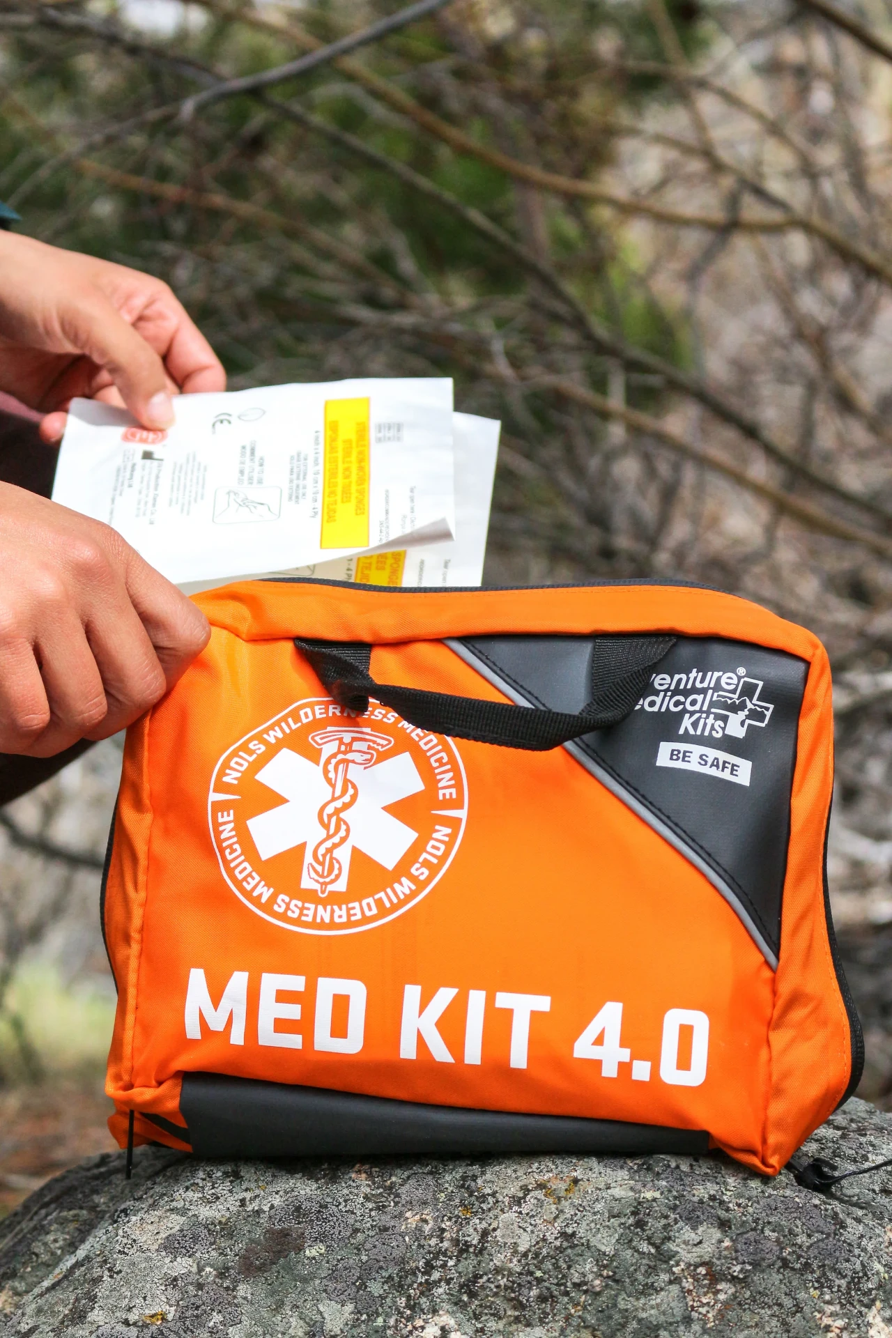 Hands opening an orange NOLS Wilderness Medicine Med Kit 4.0 on a rock outdoors